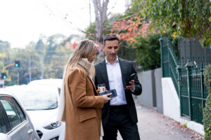 Andrew Date, Buyer Agent showing something on his phone to a woman attending an auction in South Yarra.